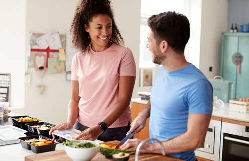 A man and woman happily preparing healthy meal preps in the kitchen, focusing on a weight maintenance meal plan for balanced nutrition.